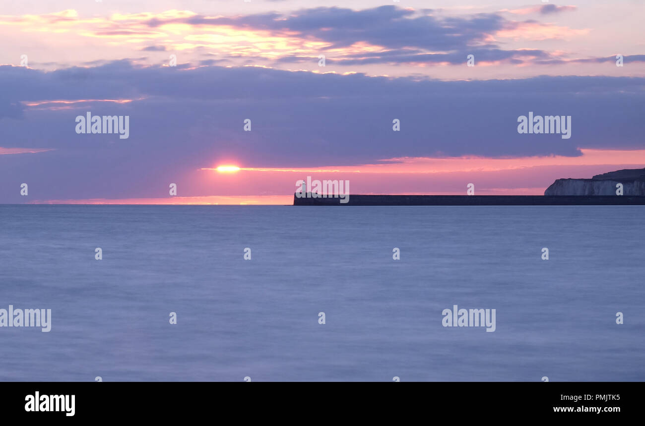 La parete del porto e Newhaven faro è proteso al centro dell'immagine behingd sono chalk scogliere e una rosa e azzurro cielo di tramonto è dietro un Foto Stock