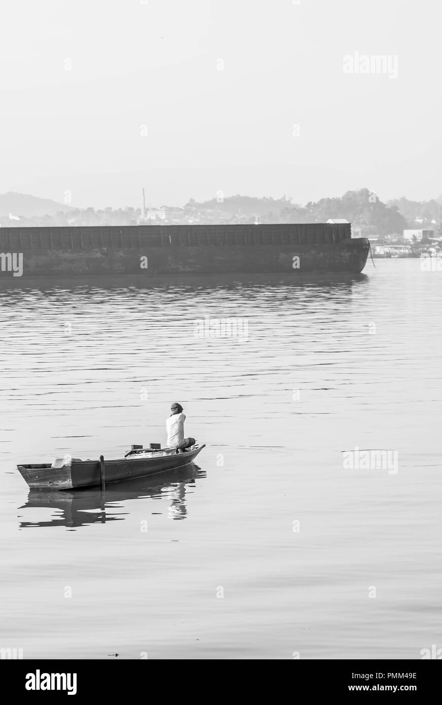 Samarinda / Indonesia - 8/19/2018 : pescatore tradizionale paddling la sua piccola imbarcazione in legno vicino la chiatta passando nel fiume Mahakam Foto Stock