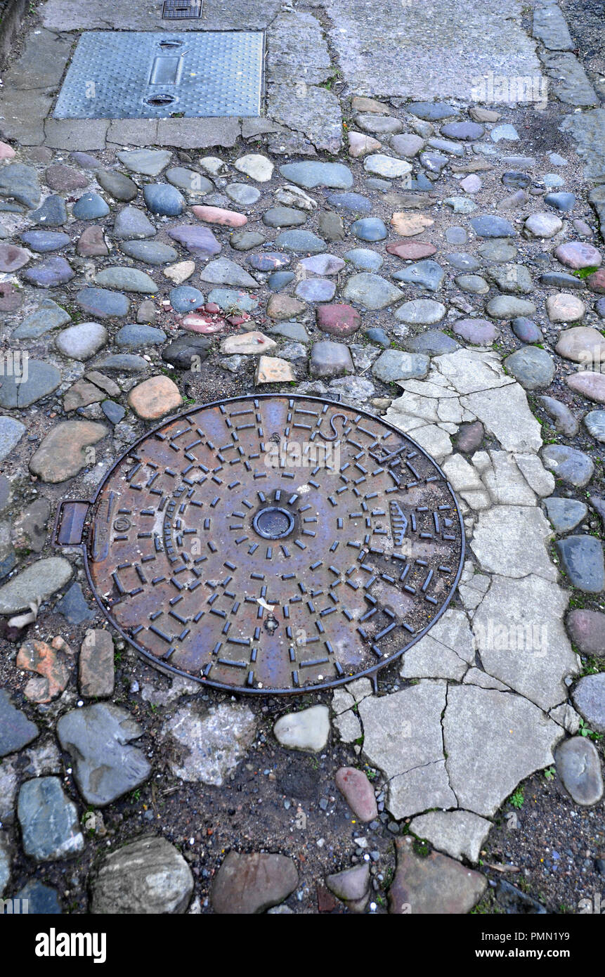 Vecchio tombino rotondo circondato da pavimentazione in ciottoli in una città di fife Scozia,UK. Foto Stock