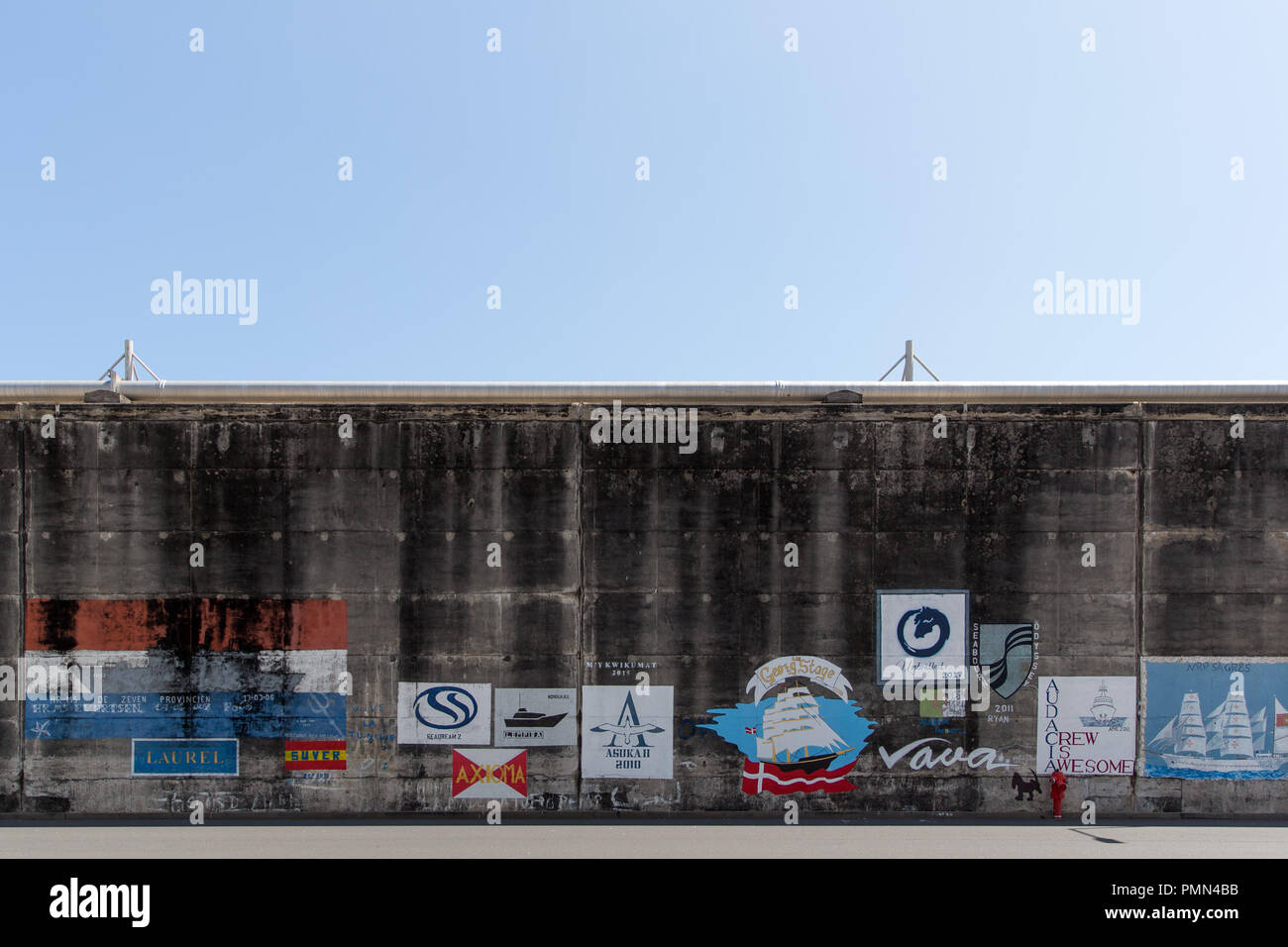 Annunci, i loghi e gli emblemi dipinta su un alto muro di cemento (mare) parete lungo la banchina del porto di Funchal, Madeira Foto Stock