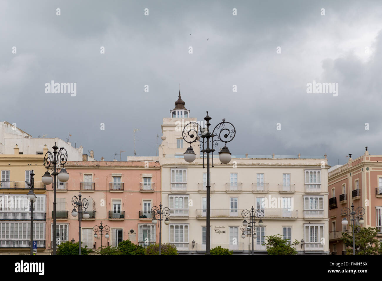 Una fila di edifici colorati e decorati intorno a una piazza principale di Cadice, in Spagna. Il cielo è grigio e nuvoloso. Foto Stock