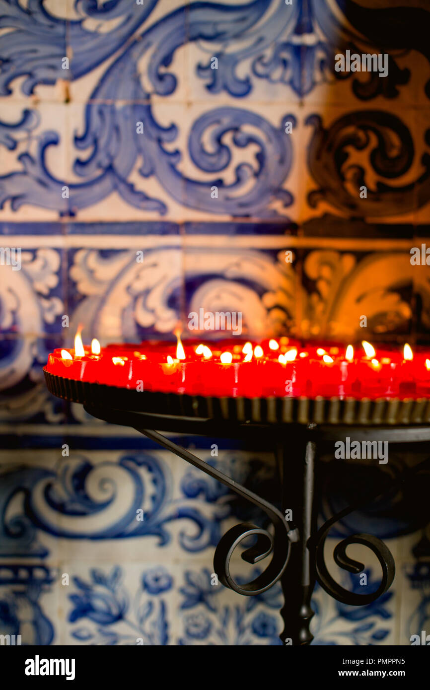 Candele votive a bruciare in una Chiesa Portoghese contro uno sfondo di colore blu e bianco delle piastrelle di ceramica (azulejos) tradizionale in Portogallo Foto Stock