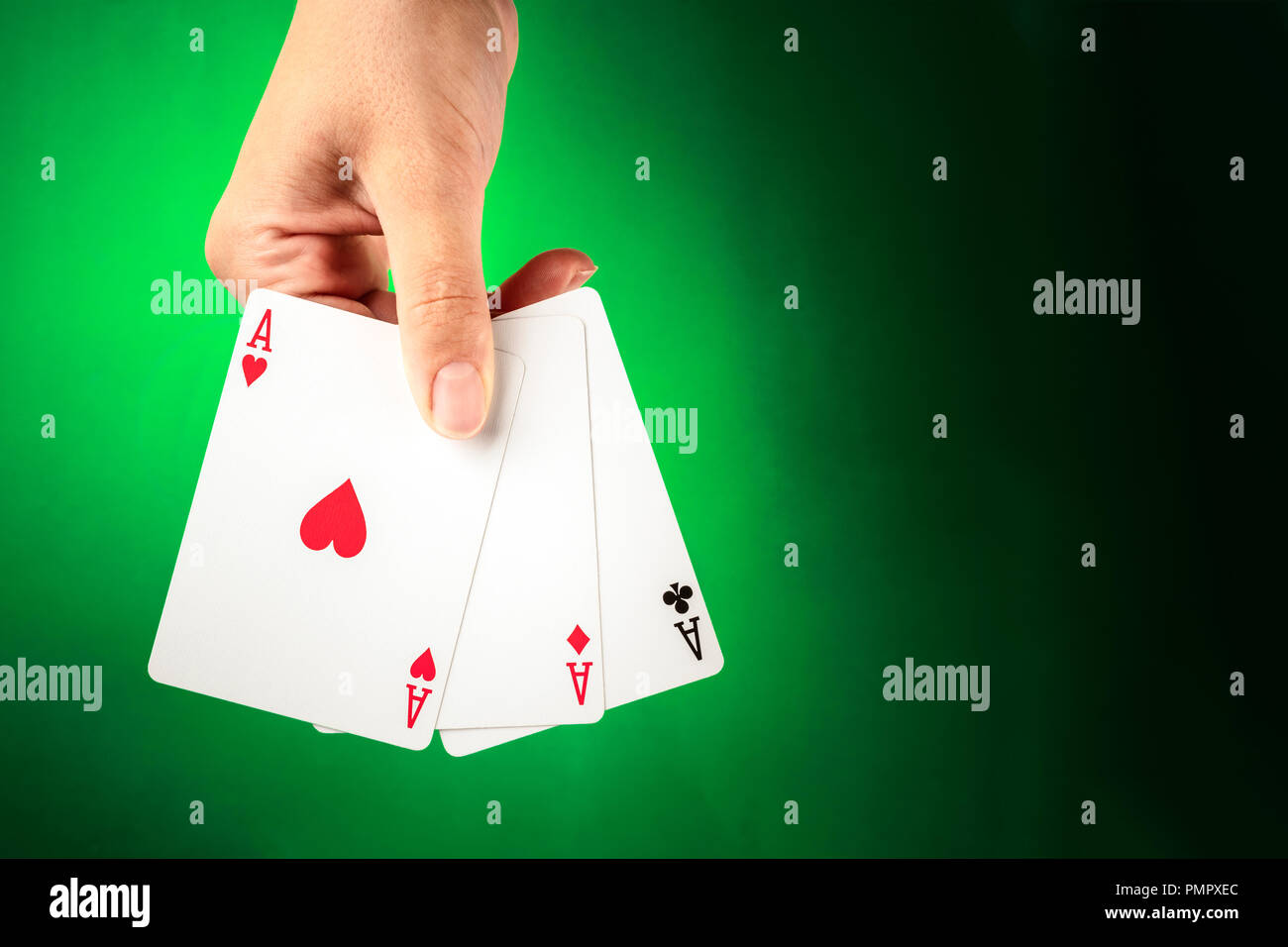Una mano che tiene tre aces contro uno sfondo verde con spazio di copia Foto Stock