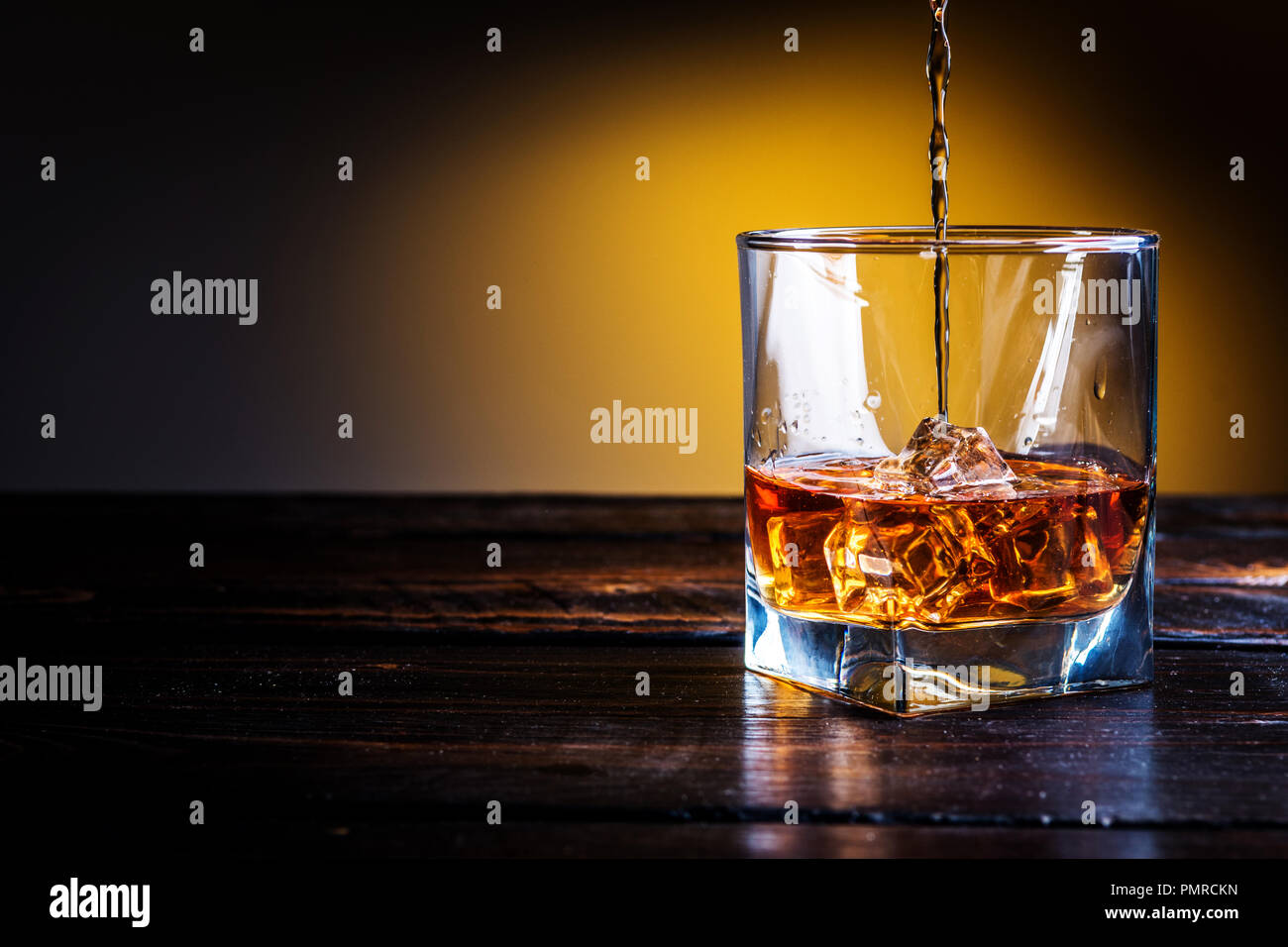 L'alcool bere whisky e whiskey Bourbon o con cubetti di ghiaccio sul legno scuro tavolo e lo sfondo arancione Foto Stock