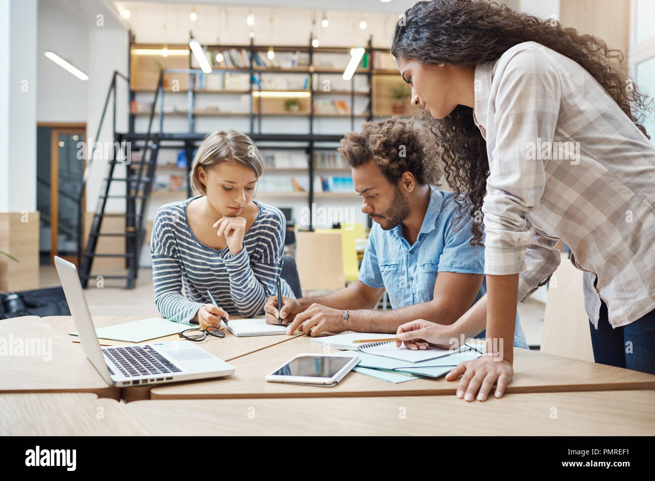 Un gruppo di tre giovani multi-etnico business di successo di persone sedute in coworking space, parlando di nuovo progetto del team concorrente, facendo piani per bypassare il loro progetto. Foto Stock