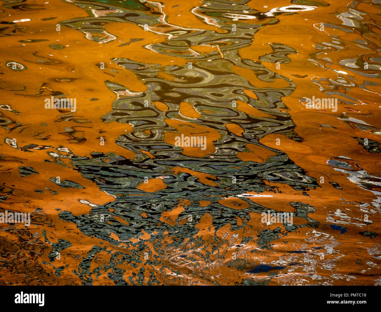 Colorato riflettente la superficie dell'acqua con dominanti di colore arancione e toni di verde. Foto Stock