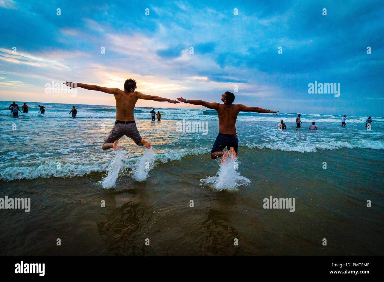 Un duo di viaggiatori che posano sulla spiaggia di Calangute durante il tramonto sulla spiaggia con cielo blu chiaro a Goa Nord, Goa, India. Foto Stock