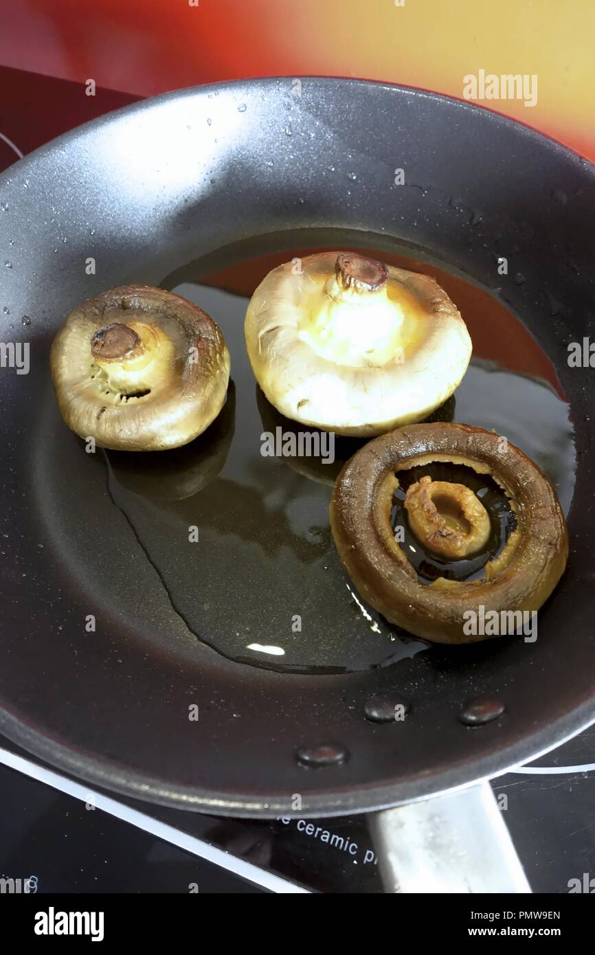 Pieno di funghi cotti in olio di oliva in una padella posta su un piano di cottura ad induzione Foto Stock