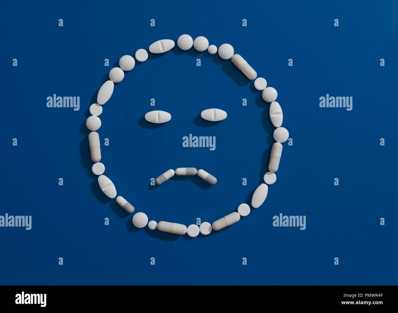 Pillole di formazione volto accigliato su sfondo blu Foto Stock