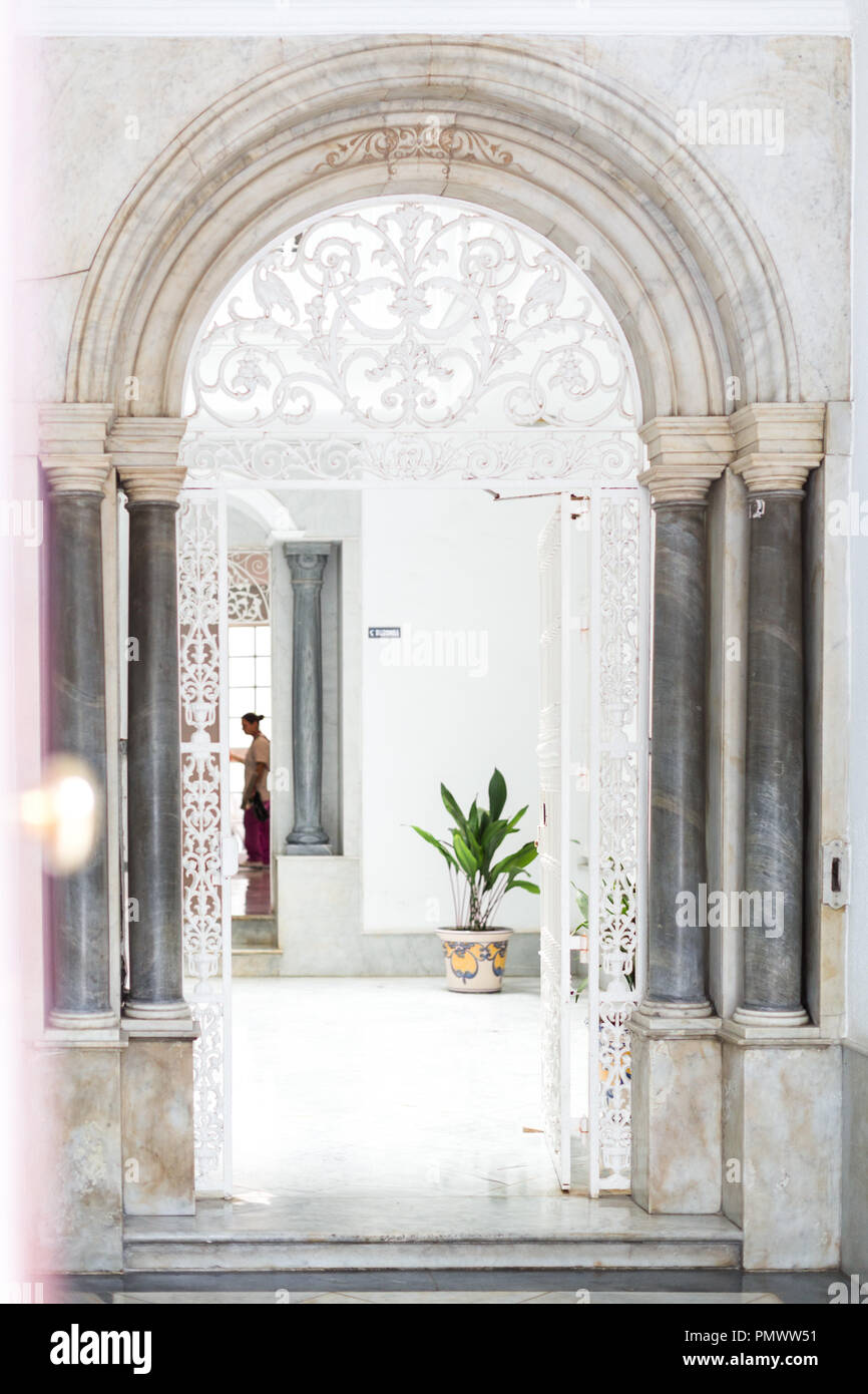 Guardando attraverso un marmo bianco porta che conduce ad un cortile interno. La porta è decorata con ferro bianco di filigrana e pilastri Foto Stock