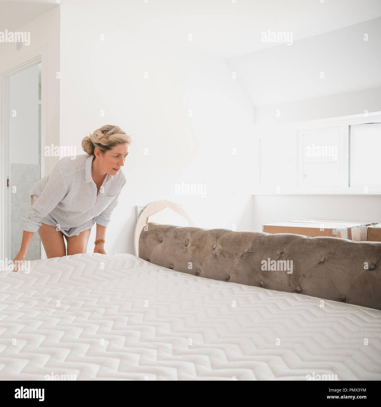 Donna matura è in movimento per la sua nuova casa. Ella sta ponendo il suo materasso sul suo letto. Foto Stock