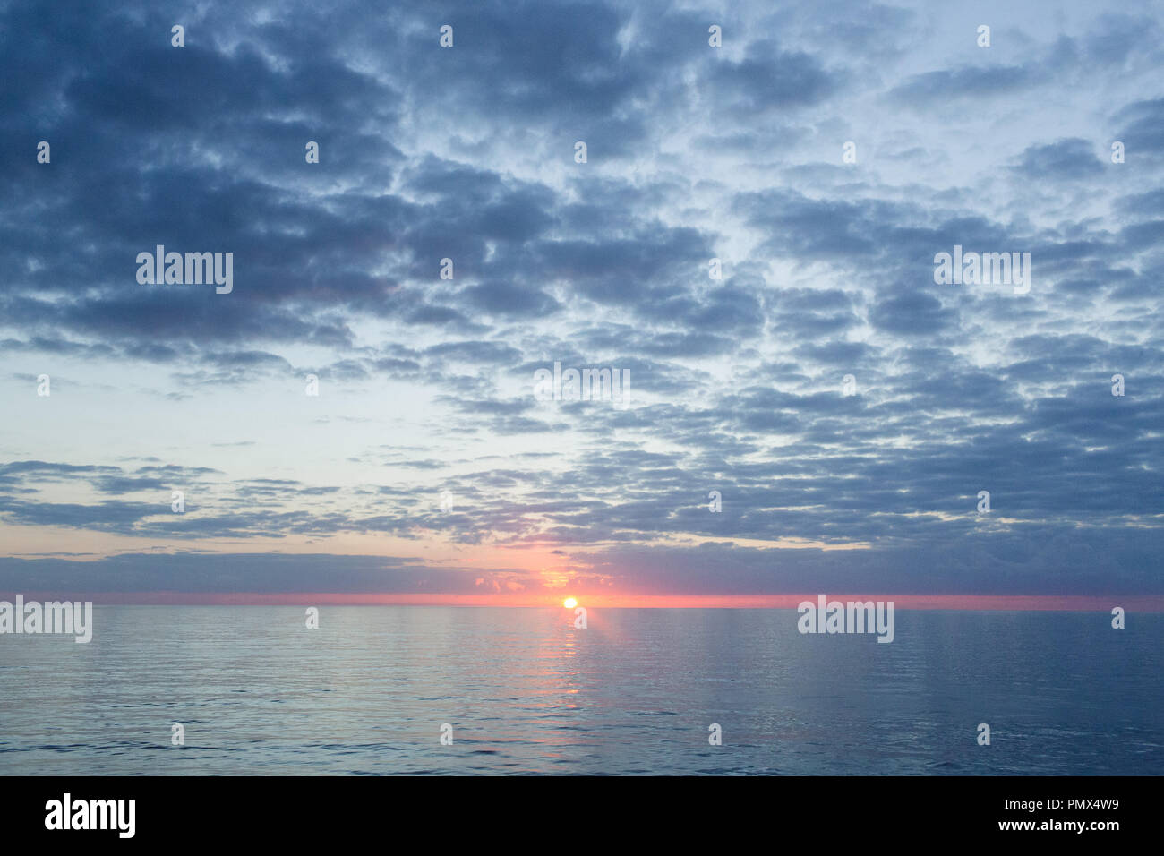 Un arancio brillante sole al centro del telaio appena al di sopra della linea di orizzonte in mare. Foto Stock