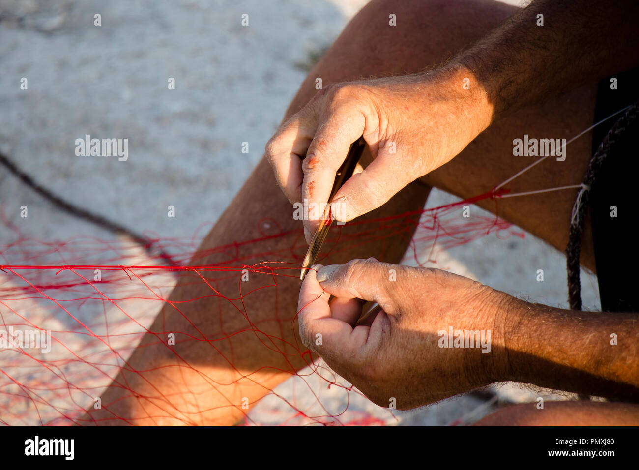 Le mani del pescatore riparando il suo rosso rete da pesca , close up dettaglio Foto Stock