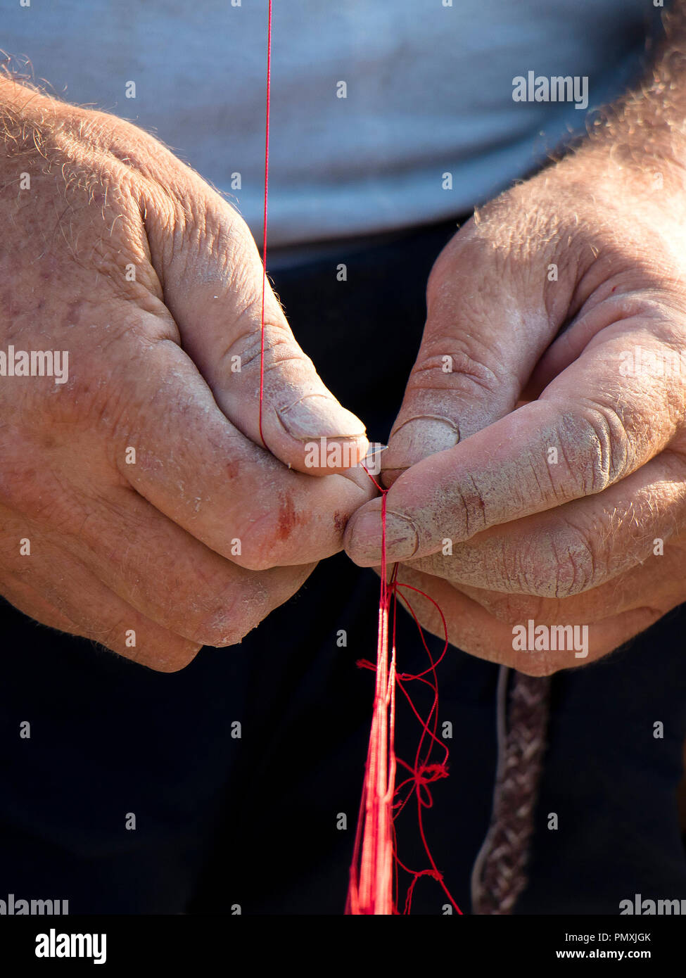 Le mani del pescatore riparando il suo rosso rete da pesca , close up dettaglio Foto Stock