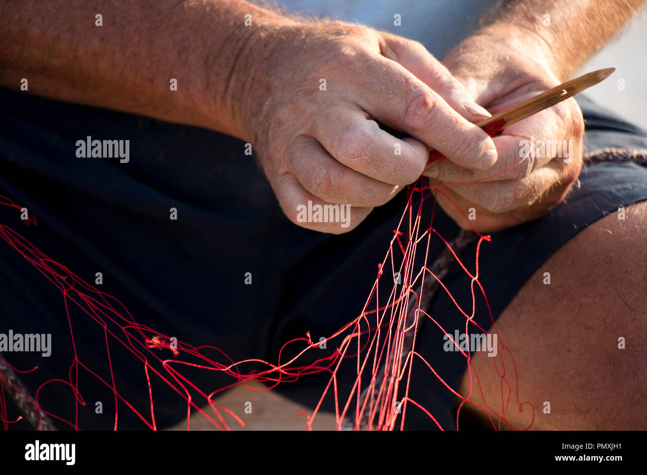 Le mani del pescatore riparando il suo rosso rete da pesca con ago , close up dettaglio Foto Stock