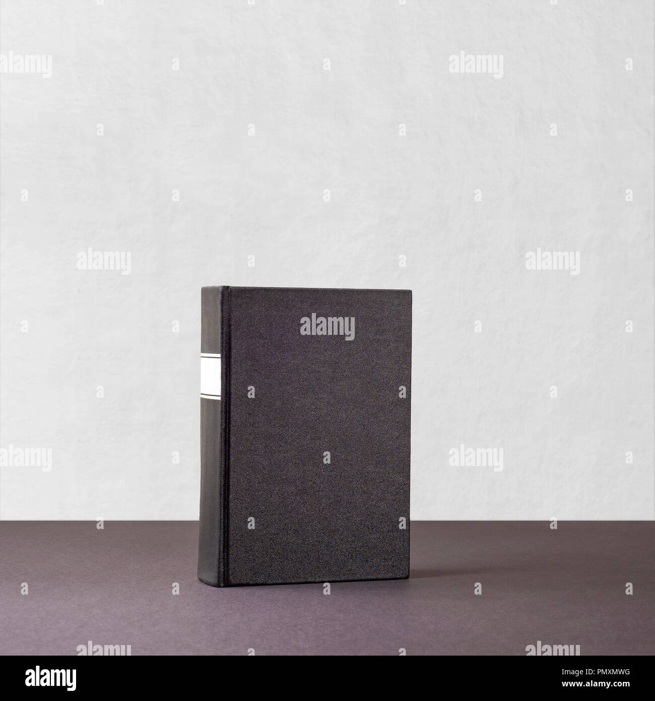 Libro nero con whiteframe sul dorso di un permanente scuro superficie di carta vicino al muro bianco Foto Stock