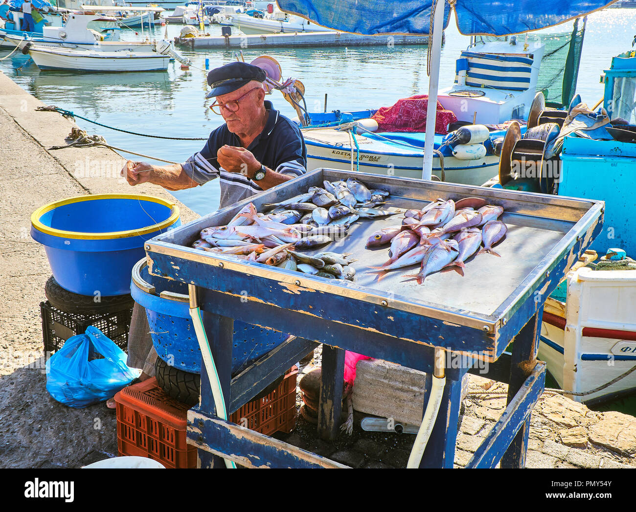 Kos, Grecia - Luglio 4, 2018. Un pescatore greco baiting ganci e vendita di pesce fresco alla Kos porto di pesca, un'isola greca del Sud Egeo regione, GRE Foto Stock