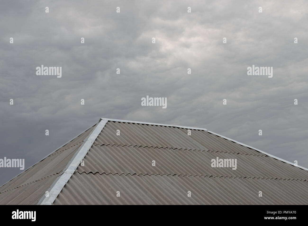 Close-up grigio in cemento-amianto foglio d'onda hip con tetto di acciaio zincati ridge e hip lampeggiante sul grigio cielo nuvoloso sfondo. Foto Stock