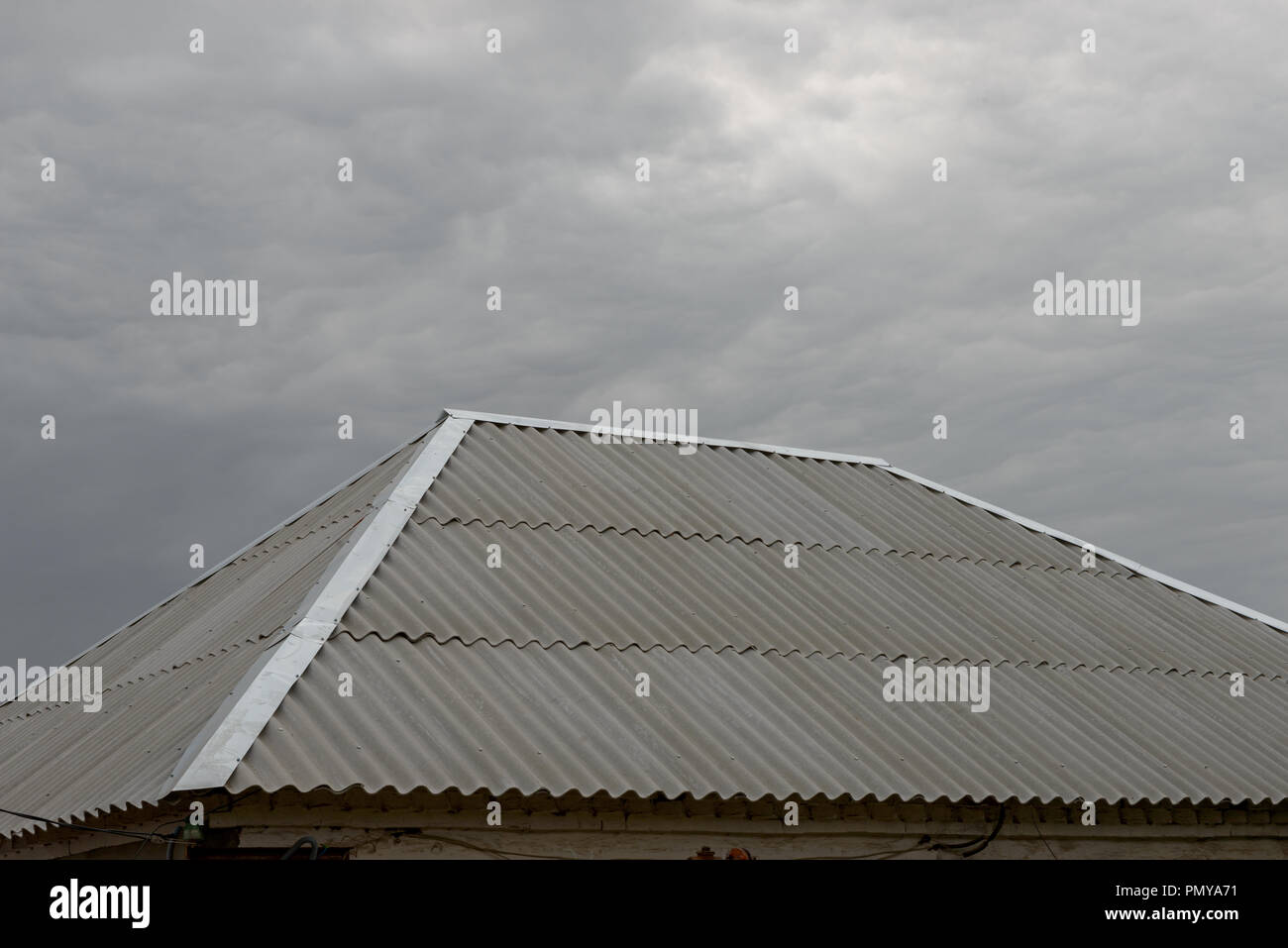 Close-up grigio in cemento-amianto foglio d'onda hip con tetto di acciaio zincati ridge e hip lampeggiante sul grigio cielo nuvoloso sfondo. Foto Stock