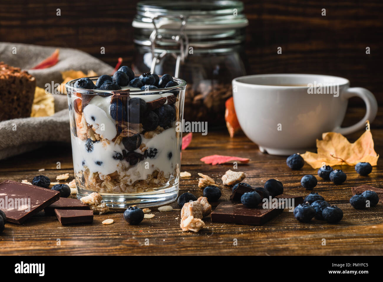 Muesli con yogurt, mirtilli, miele e barrette di cioccolato. E la tazza di caffè sul fondale. Foto Stock