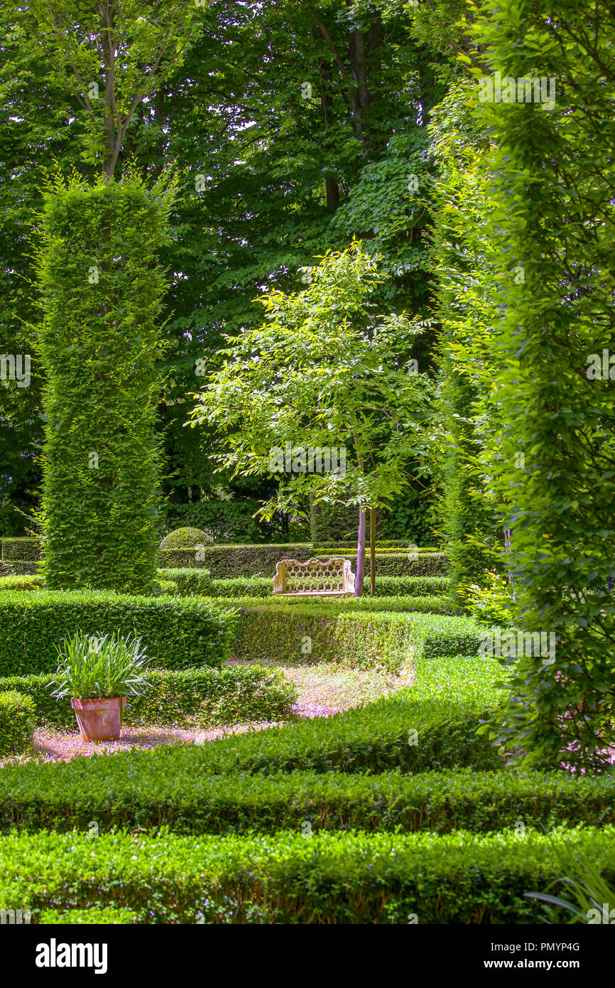 Un bel verde e lussureggiante giardino soleggiato con una panca in legno Foto Stock