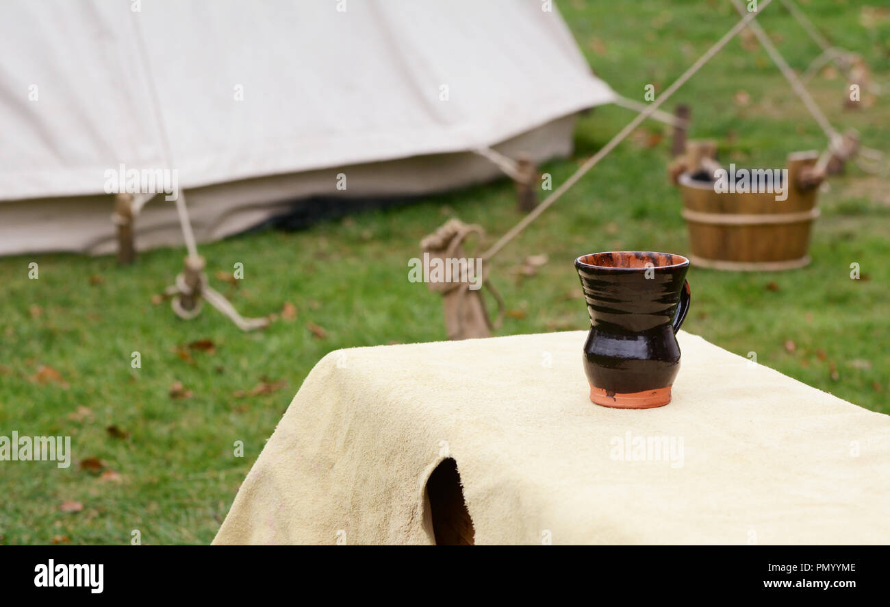 In argilla smaltate cup sorge su una panchina coperta con una pelle di camoscio in un accampamento medievale di impostazione Foto Stock