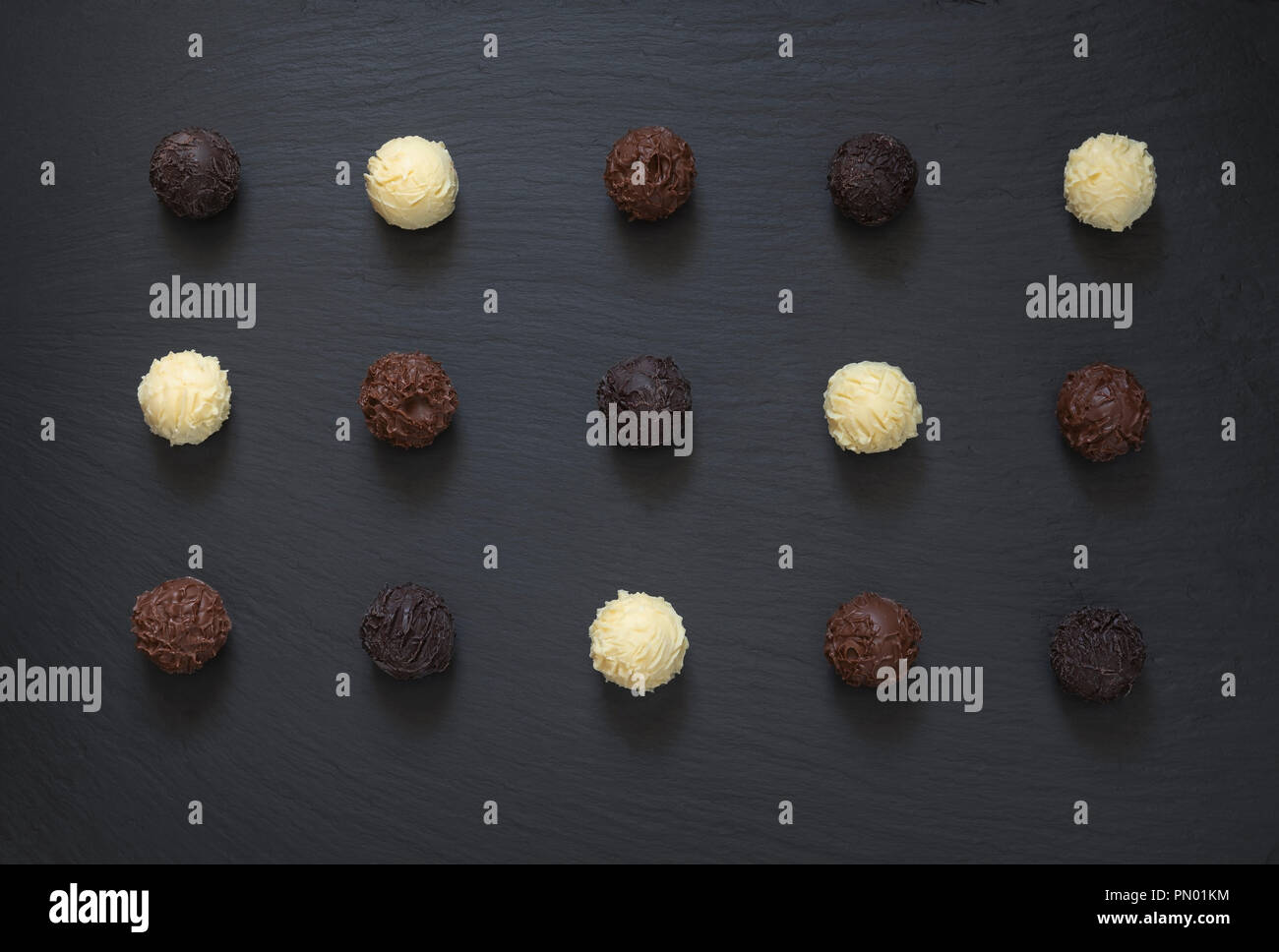 Fancy scuro bianco latte tartufi di cioccolato pronto a mangiare sulla pietra nera dello sfondo. Foto Stock