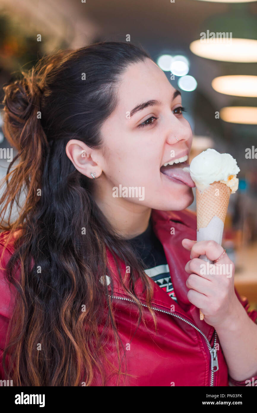 Giovani brunette con capelli lunghi donna ragazza mangiare con gelato alla vaniglia con rosso giacca di pelle ritratto Foto Stock