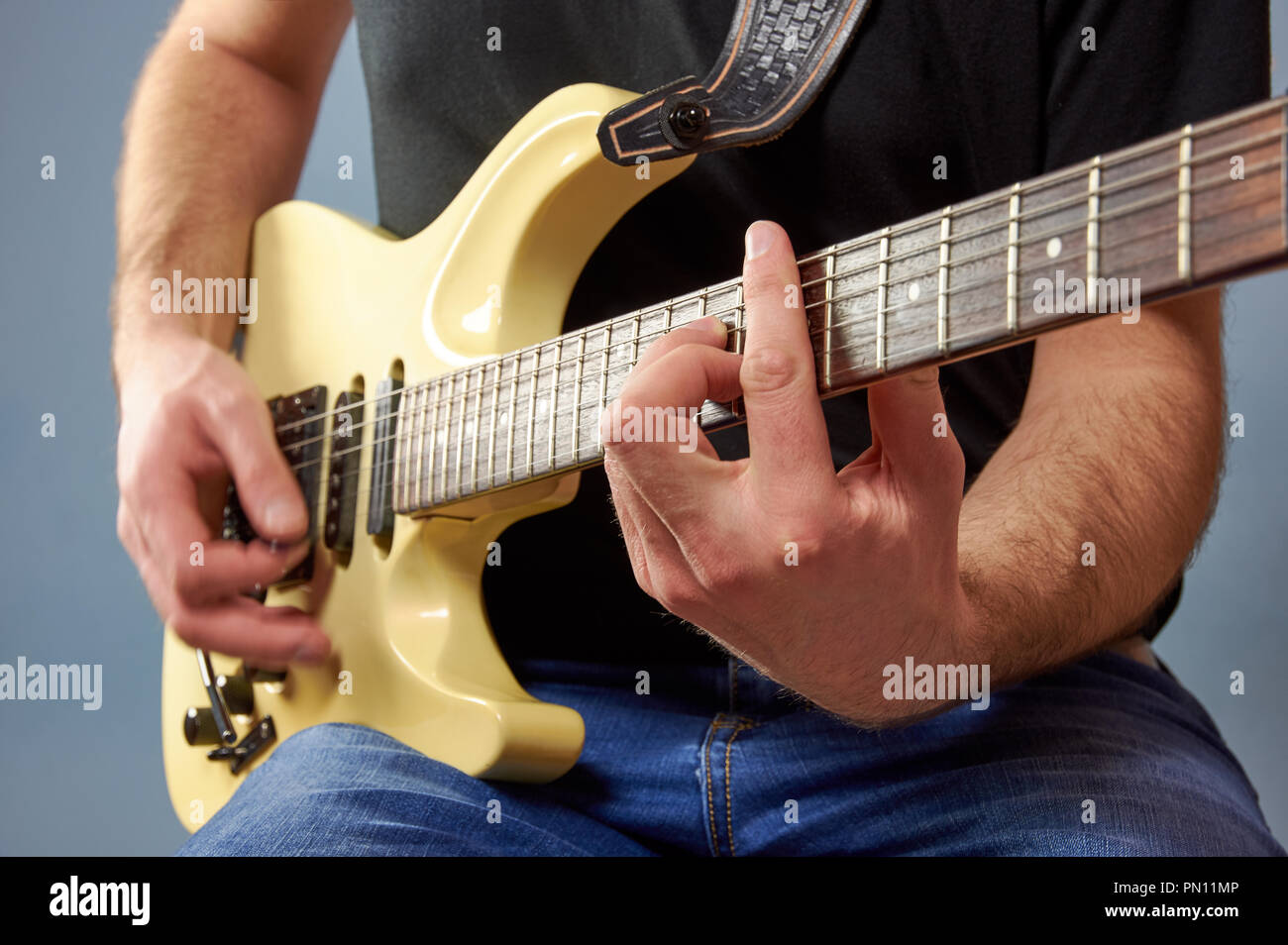 Un Uomo in camicia nera e jeans suonando una chitarra elettrica. Dita dettaglio, sfondo blu. Foto Stock