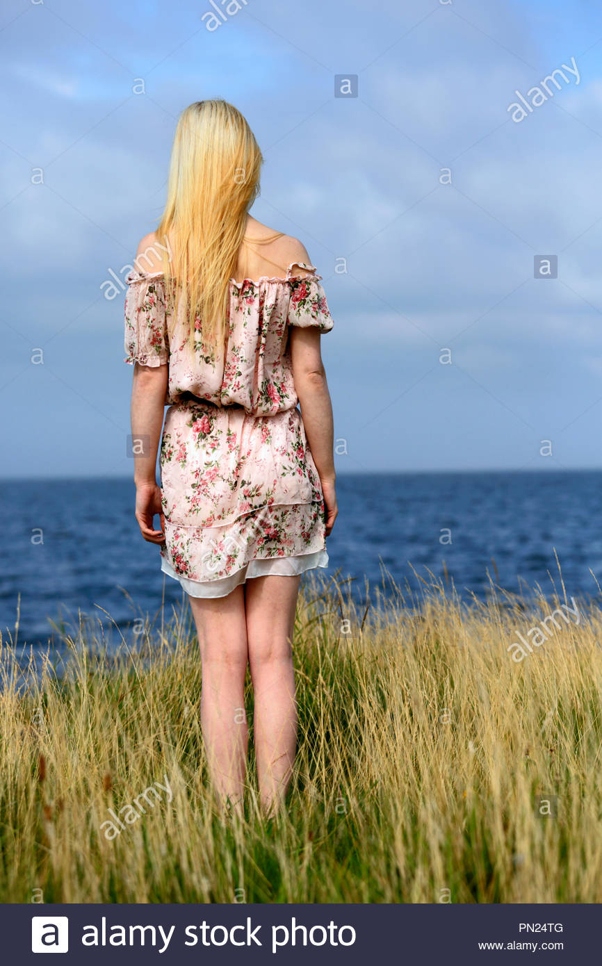Donna bionda in abiti estivi che guarda al mare Foto Stock