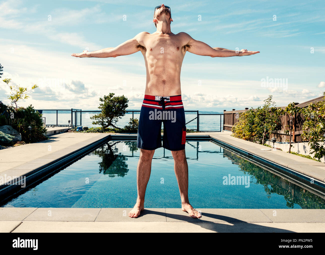 Uomo accanto alla piscina con le braccia sollevate guardando al cielo in soggezione Foto Stock