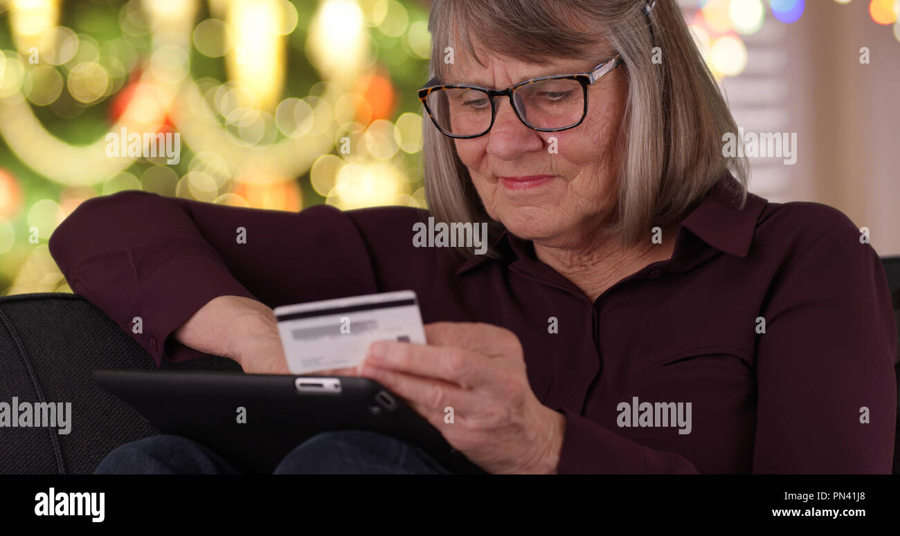Stretto colpo di felice old Lady sul lettino shopping di Natale online utilizzando il dispositivo tampone Foto Stock