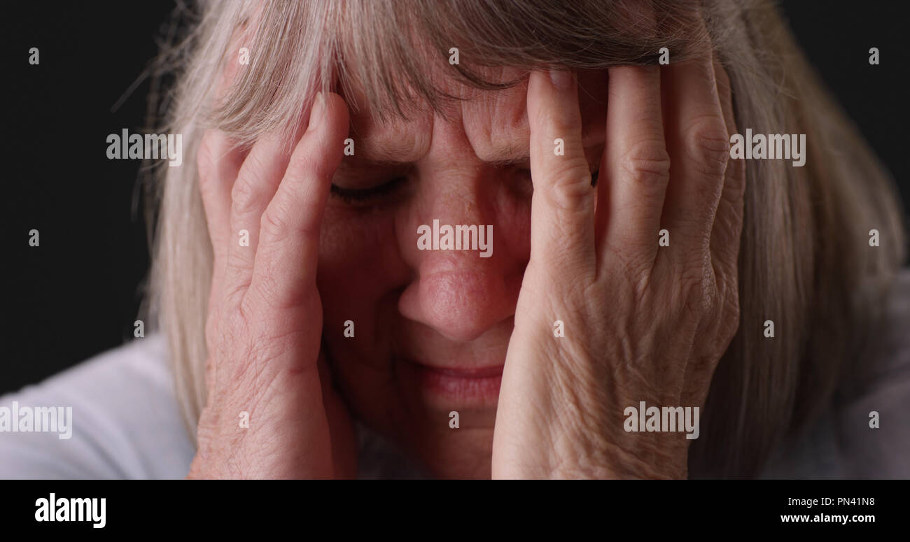 Stretto colpo di donna anziana con il mal di testa di emicrania testa di sfregamento su sfondo grigio Foto Stock