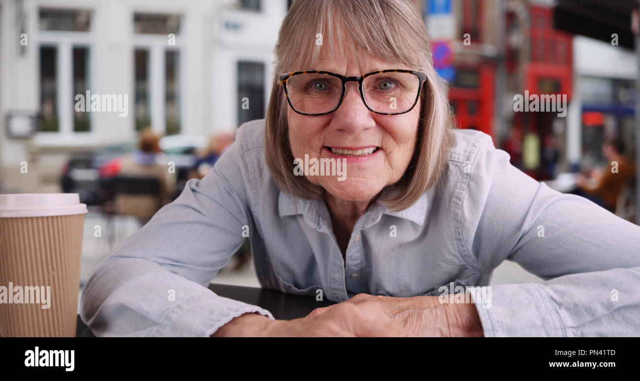 Close up di senior donna sorridente alla telecamera fuori cafe in città europea Foto Stock