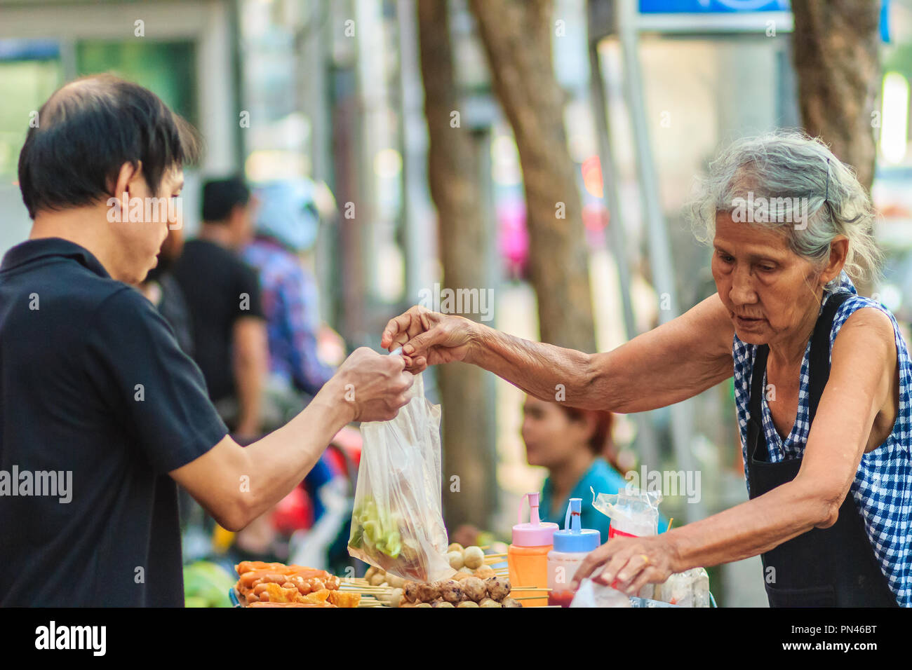 Bangkok, Tailandia - 23 Aprile 2017: Unidentified vecchia donna street vendor è la vendita di carne fritta delle sfere per il suo cliente. Foto Stock