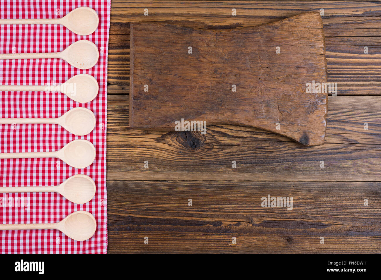 Vecchi rustici di legno con sfondo rosso bianco panno a scacchi. Sul tessuto sono di legno mestoli in una fila. Con copia spazio su una vecchia scheda di taglio Foto Stock