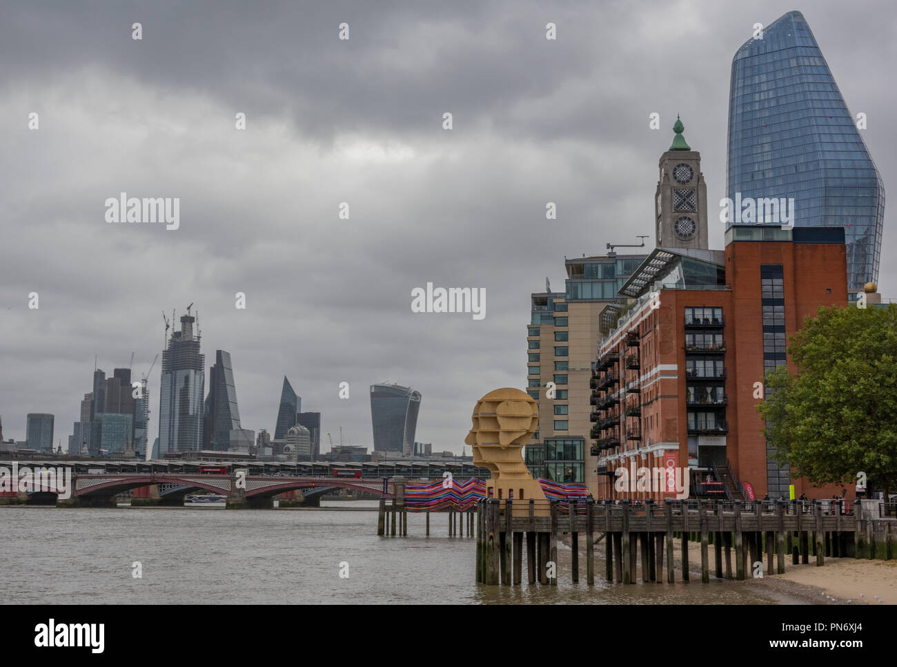 Londra, Regno Unito. Xx Settembre 2018. La skyline di Londra e installazioni di arte alla giunzione di design, parte della London Design Festival sulla riva sud del fiume Tamigi in centro a Londra presso la torre di osso. La colorata 'gateway per inclusione' e la scultura in legno "testa sopra l'acqua elevare il profilo delle questioni concernenti la salute mentale nel Regno Unito. Una tipica giornata autunnale con il grigio nuvole sopra la città di Londra fornisce lo sfondo e lo skyline in un suggestivo paesaggio di Londra. Foto Stock