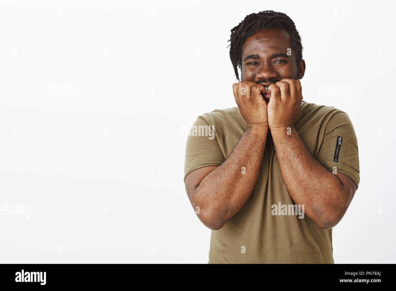 Wais-up shot di impaziente bella afro-americano in costume militare, tenendo le mani su palme e sorridente largamente, in attesa di sorpresa positiva e grinning, in piedi felice su muro grigio Foto Stock