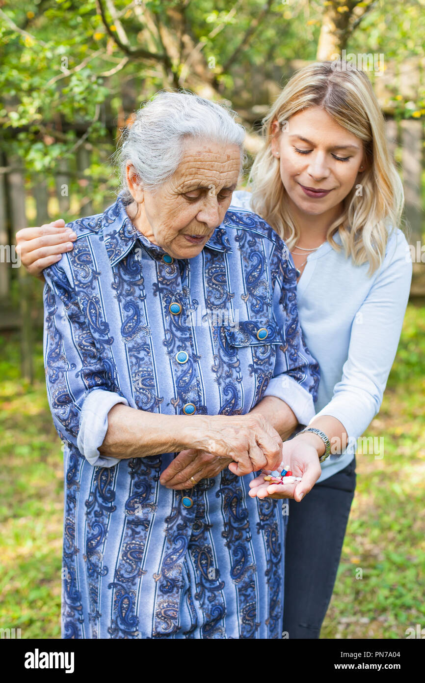 Disabilitato old Lady tenendo medical pillole dal caregiver amichevole la mano. Trascorrere il tempo in giardino Foto Stock