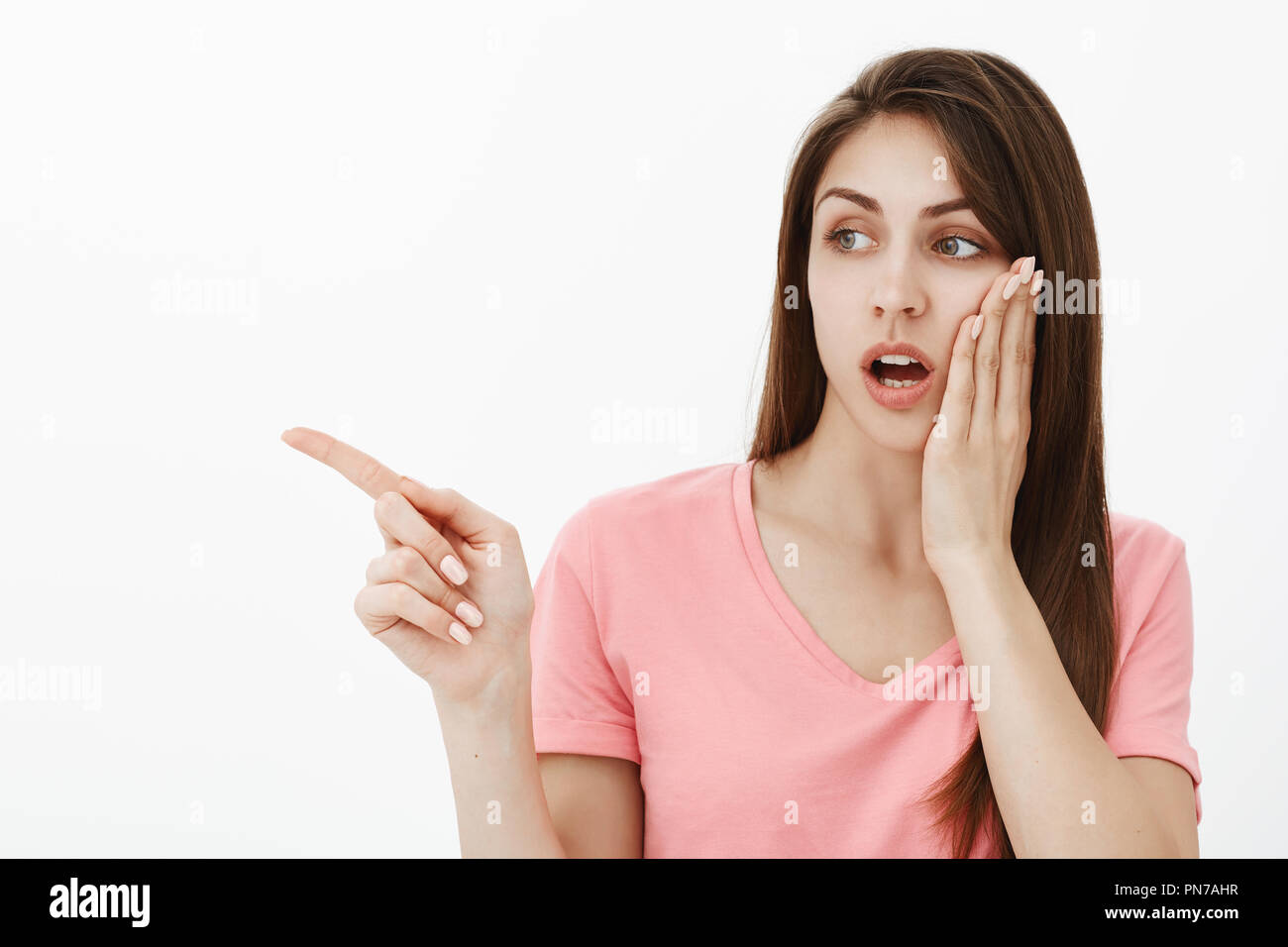 Gosh, basta guardare ciò che ella usura. Ritratto di scioccato europea femminile in rosa t-shirt, tenendo palm sulla guancia e mascella caduta mentre cercano e rivolta a sinistra, spettegolare e diffusione di voci Foto Stock