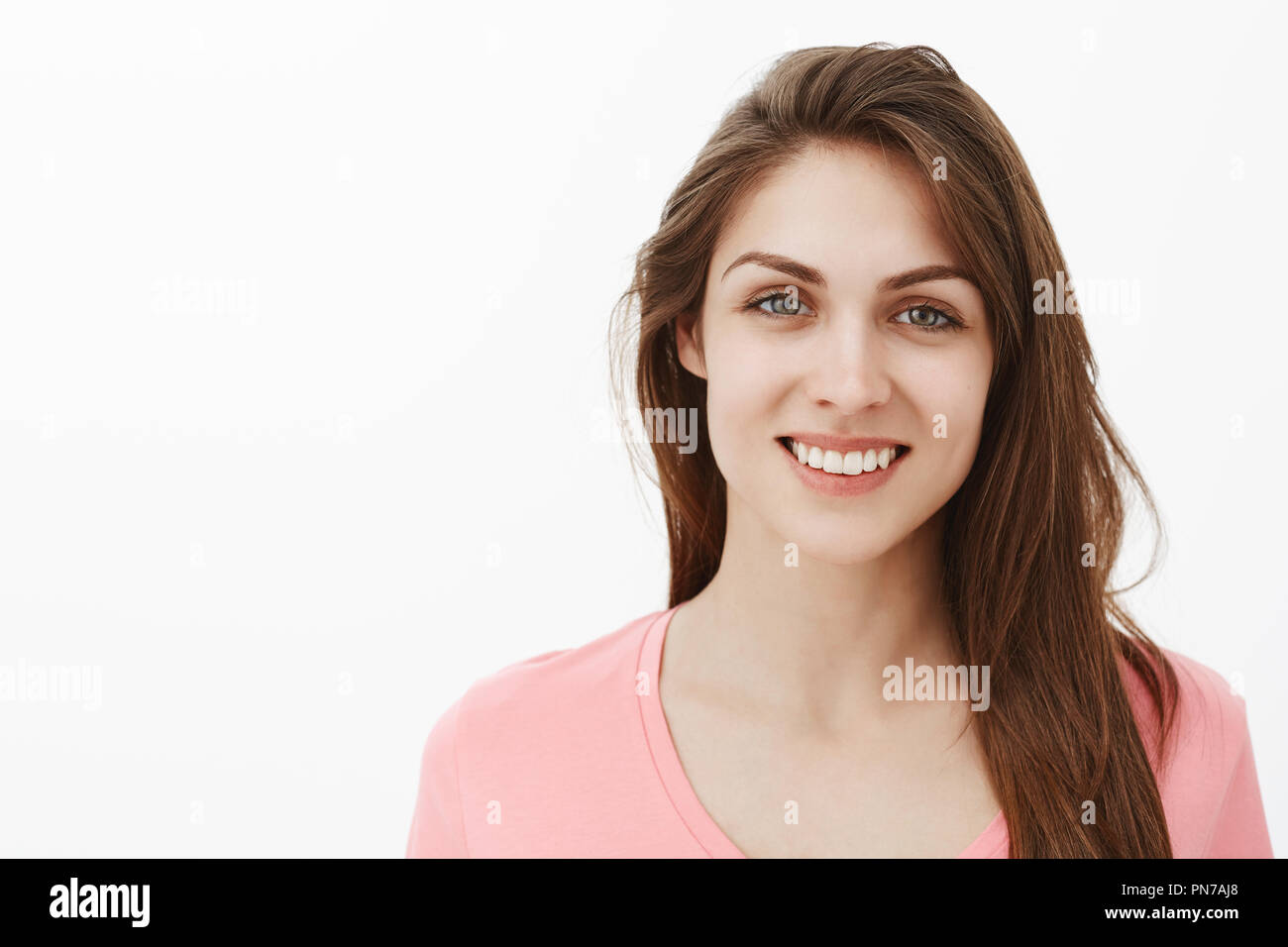 Close-up shot di cordiale donna comunicativa in t-shirt rosa, sorridente con gioia e guardando con attenzione e calorosa manifestazione in telecamera, in piedi su uno sfondo grigio, femminile e dolce Foto Stock