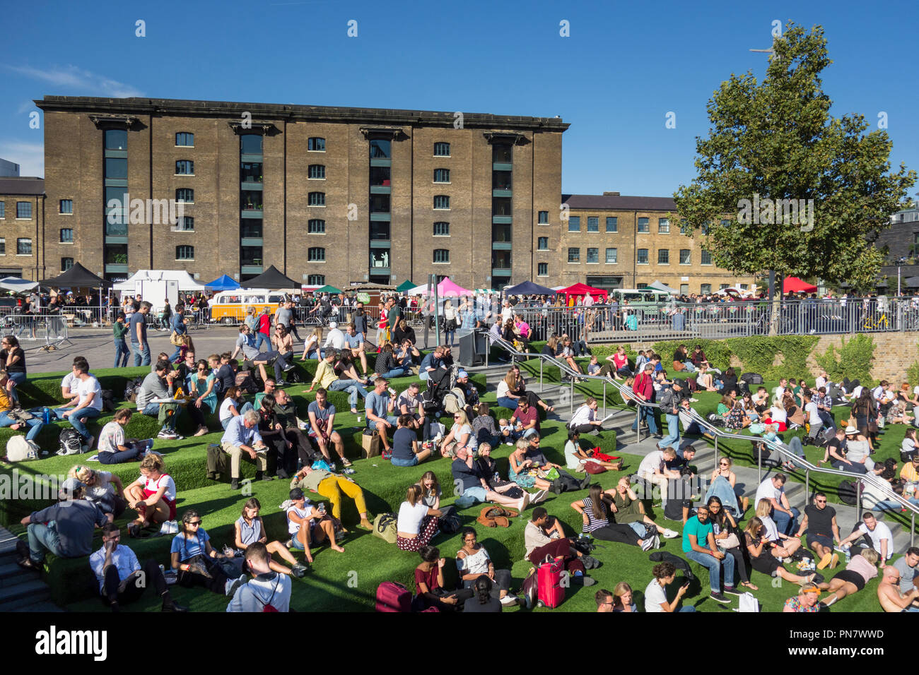 Folle di persone che prendono il sole fuori dal canalside e il Granary Building a Granary Square, King's Cross, Camden, Londra, N1, Inghilterra, Regno Unito Foto Stock