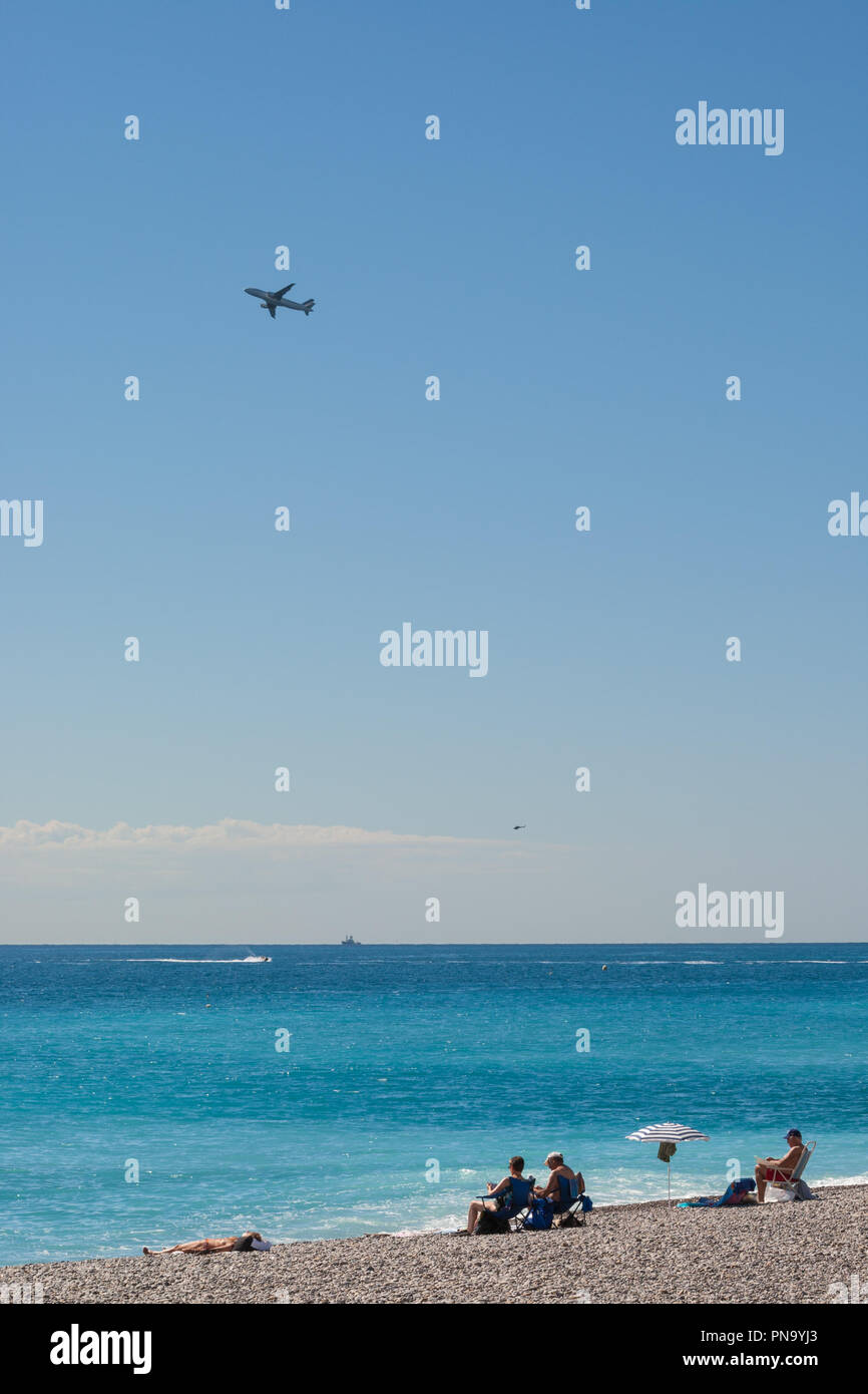 Promenade des Anglais, Nice, Francia - Settembre 2012 : i turisti sulla spiaggia di ciottoli e di un aereo in fase di decollo. Foto Stock