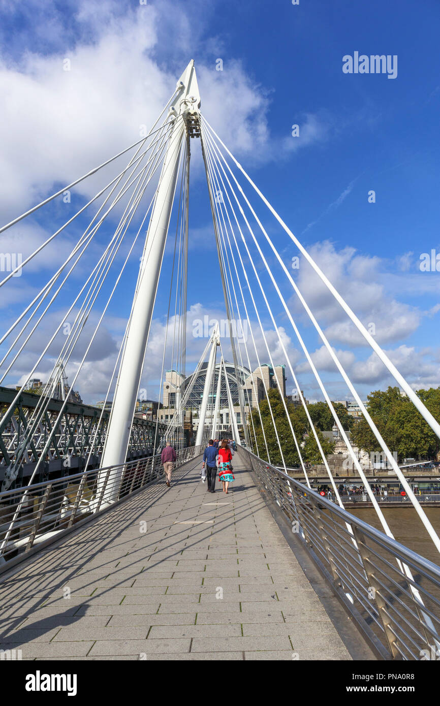 Cavo moderna-alloggiato il Golden Jubilee Bridge da Hungerford ponte sopra il fiume Tamigi, Charing Cross Station dietro su un soleggiato nella tarda estate del giorno Foto Stock