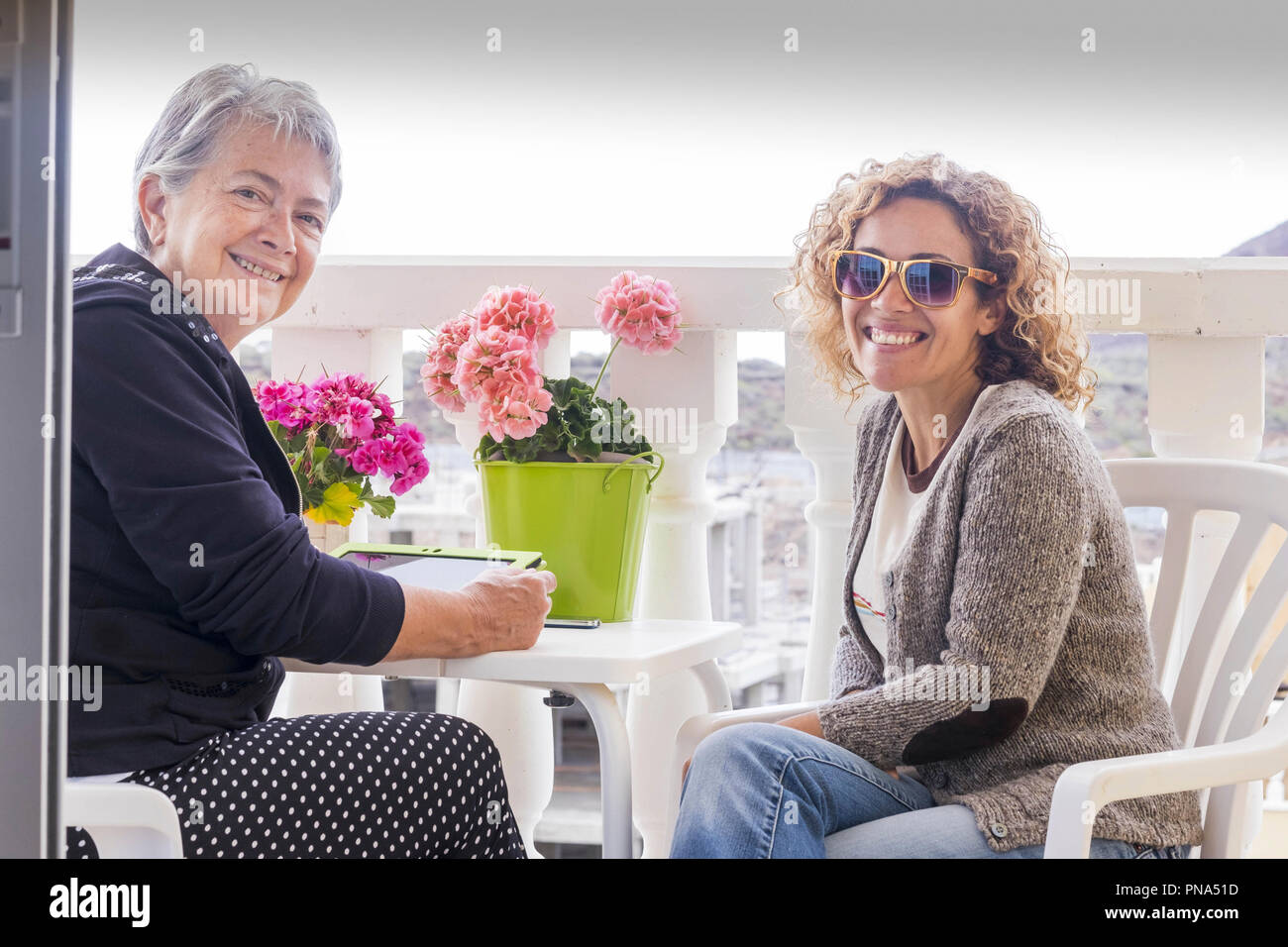 Coppia di donne amici soggiornare in terrazza insieme godendo l'amicizia a casa. utilizzando technlogy connesso a internet tablet e sorriso al camer Foto Stock