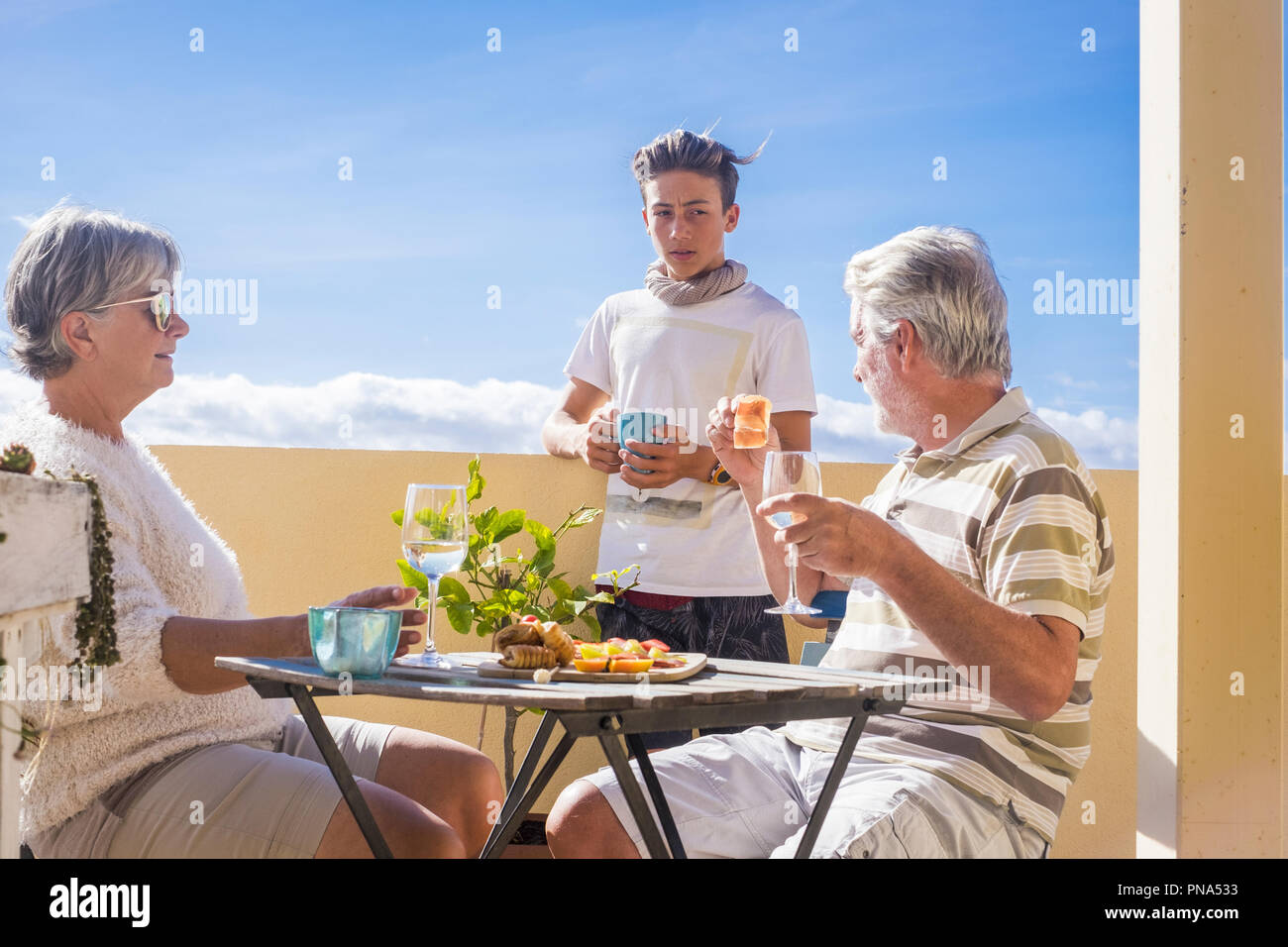 Nonni adulta e matura adolescente nipote gustare all'aperto in terrazza qualche tempo libero con cibo e bevande. oceano e vista sulla città, vacanza soleggiata da Foto Stock