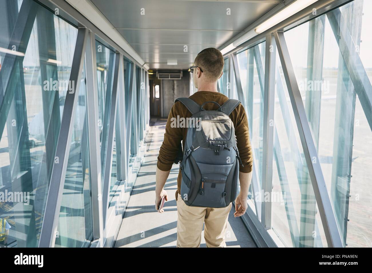Viaggiare in aereo. Vista posteriore del giovane con zaino e passaporto in mano durante l'imbarco in aeroporto. Foto Stock