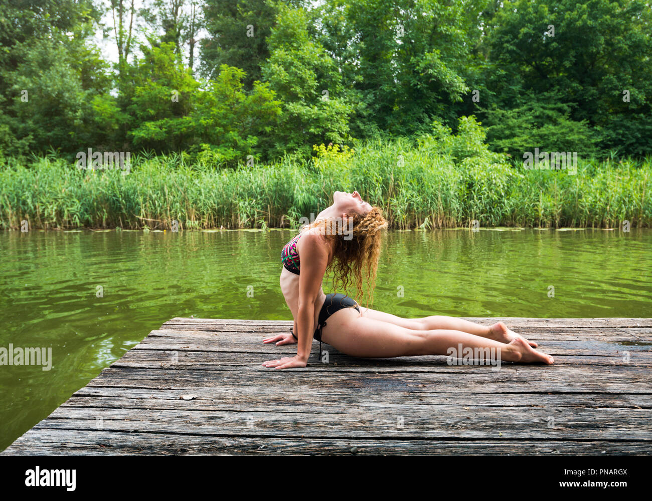 La donna a praticare yoga sul dock dal lago in posa Cobra Foto Stock
