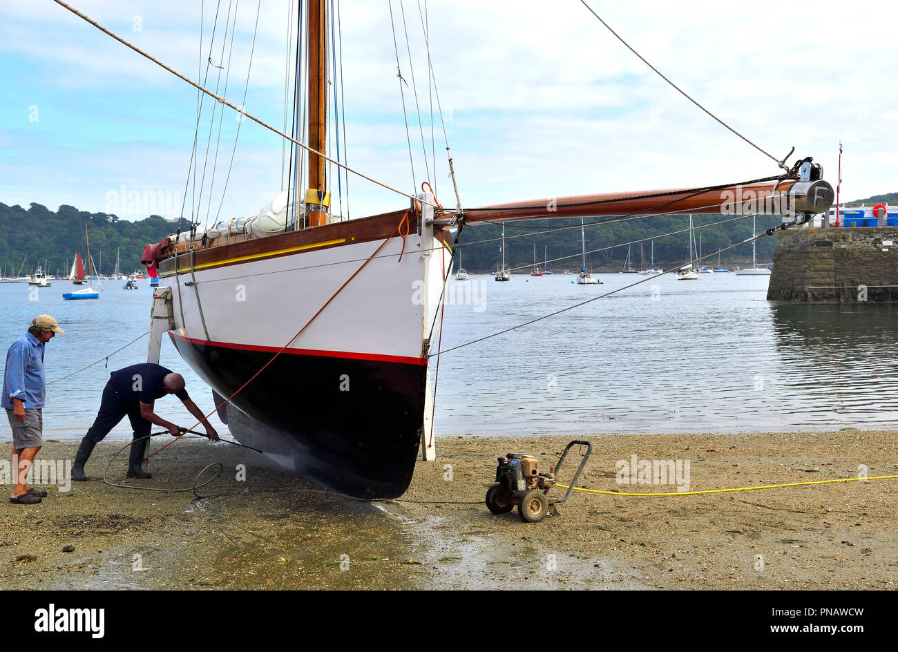 Lavaggio di potenza dello scafo di un lavoro Falmouth barca sulla spiaggia di St Mawes, penisola di Roseland, Cornwall, South West England, Regno Unito Foto Stock