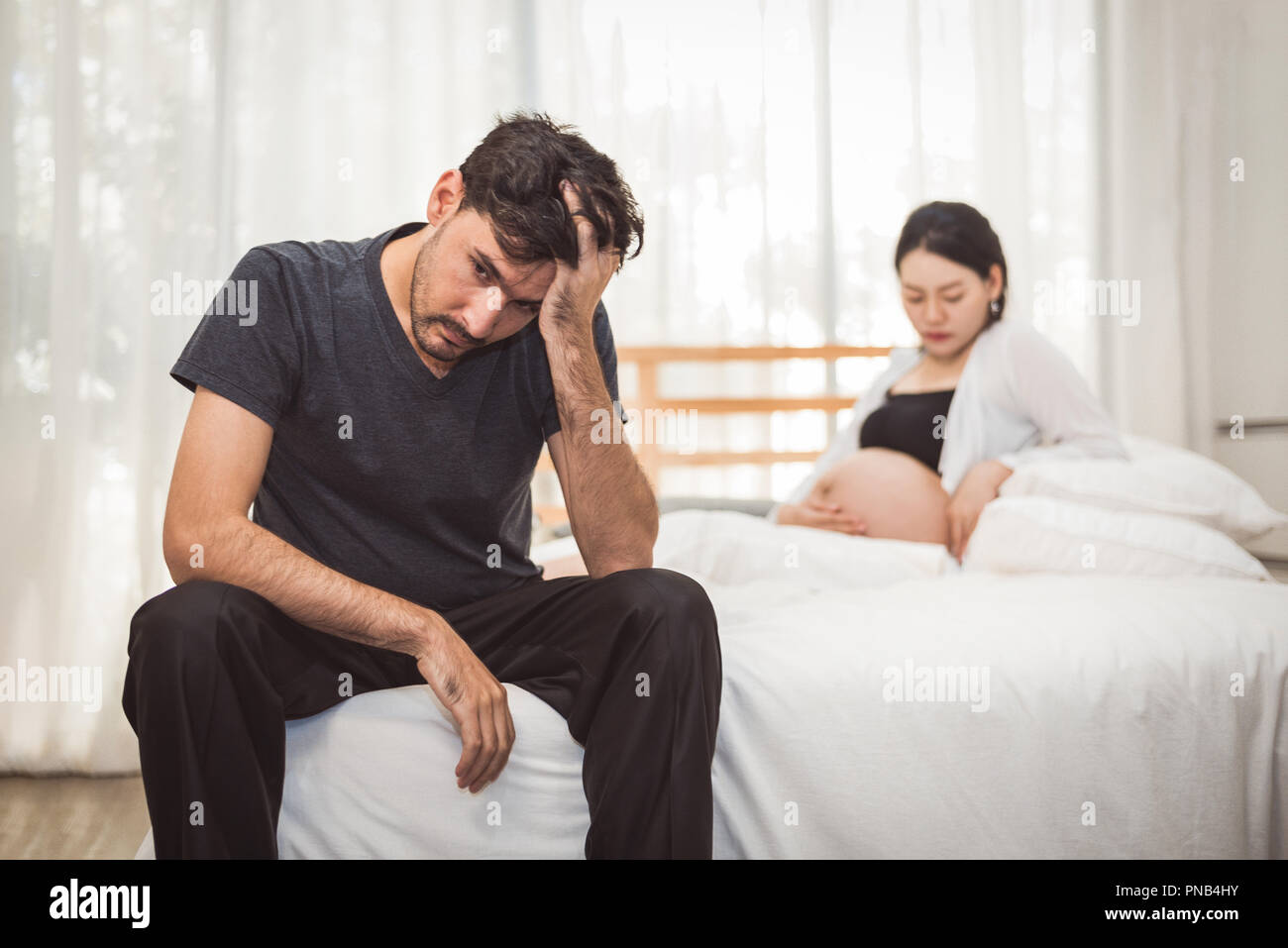 Preoccupato stress uomo seduto sul letto con la mano sulla fronte in camera da letto in gravi umore emozione con moglie incinta Donna sfondo. Depressivi maggiori Disor Foto Stock